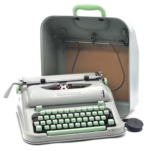 May include: A vintage light grey Hermes typewriter with mint green keys and accents, next to its matching carrying case. The typewriter features the brand name "HERMES". The case has a green handle. The typewriter is a classic writing tool.