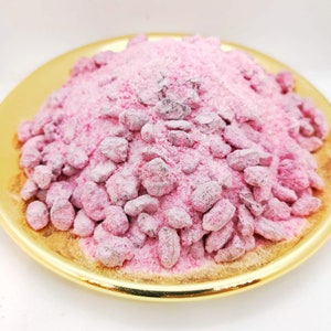 May include: A close-up of a pink incense powder with small, dark brown pieces mixed in. The powder is in a gold-coloured dish.