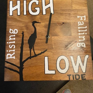 May include: Wooden sign with a black silhouette of a heron on a branch. The sign reads "HIGH TIDE" and "LOW TIDE" with "Rising" and "Falling" written vertically on either side of the heron.