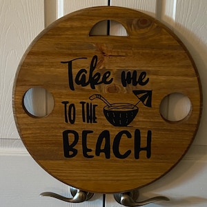 May include: A round wooden serving tray with a cutout handle and two drink holders. The tray has a black vinyl decal that says "Take me to the beach" with a coconut drink and umbrella graphic.