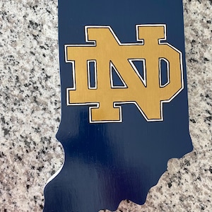 May include: A blue wooden cutout of the state of Indiana with a gold and white "ND" logo in the center.