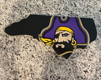 May include: A black and purple wooden cutout of the state of North Carolina with the North Carolina State University mascot, a pirate, in the center.