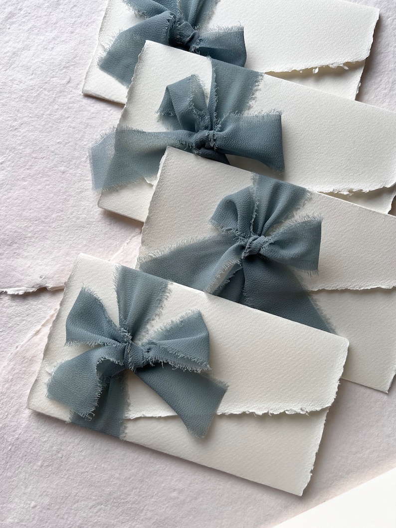 May include: Four white envelopes with frayed edges, each tied with a dusty blue ribbon bow.