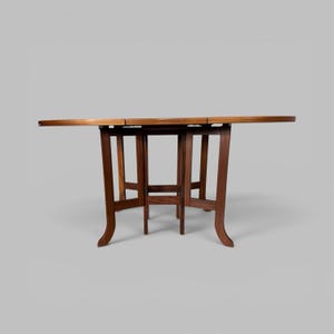 May include: A round wooden drop-leaf table with a smooth, polished dark brown finish. The table features a central support structure with four curved legs that extend outwards, providing stability for the circular tabletop surface.