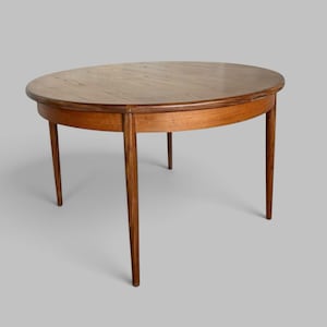 May include: A round wooden dining table with a smooth, medium-brown grain finish. The table features a circular top with a slightly rounded edge and four tapered, cylindrical legs that extend outward from the centre frame to the floor.