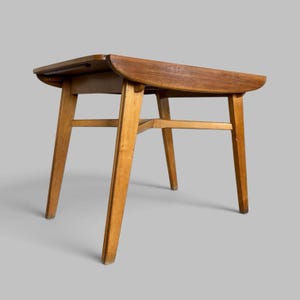 May include: A wooden side table with a rectangular top featuring rounded edges and a smooth brown finish. The table is supported by four tapered legs connected by a central cross-brace structure, showcasing a natural wood grain texture throughout.