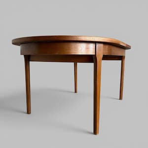 May include: A mid-century modern, round wooden table with a warm brown finish. The table has a curved edge and four slender, tapered legs. The table is approximately 76 cm in diameter.