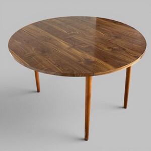 May include: A round dining table featuring a polished dark brown wood grain surface with visible natural patterns. The table is supported by three slender, tapered cylindrical legs in a lighter brown wood finish, providing a stable base.