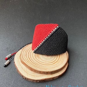 Puede incluir: Un brazalete trenzado negro y rojo con cuentas plateadas. El brazalete está sobre una superficie de madera.