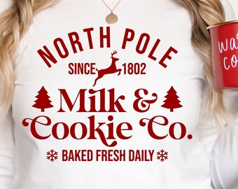 May include: A white long-sleeved shirt with a red graphic that says "North Pole Since 1802 Milk & Cookie Co. *Baked Fresh Daily*" with a reindeer and Christmas tree illustrations.