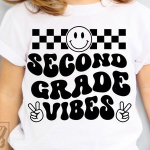 May include: White t-shirt with black text that reads "Second Grade Vibes" in a retro font. A smiley face and checkered pattern are above the text. Peace signs are on either side of the text.