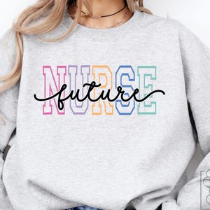 May include: A light gray sweatshirt with the words "NURSE future" in a colorful, collegiate-style font. The word "future" is in a cursive script. The sweatshirt has long sleeves and a crew neck.