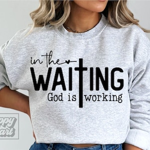 May include: A gray sweatshirt with the text "in the waiting God is working" printed on it. A small heart and a cross are included in the design.