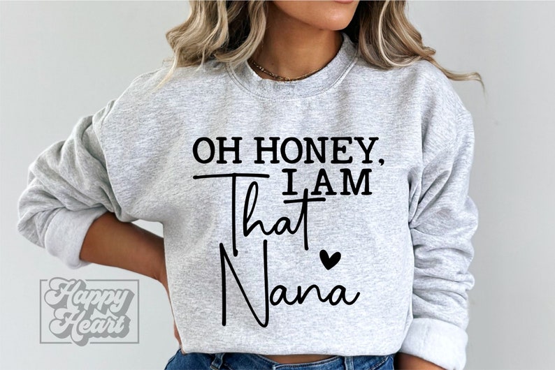 K&ouml;nnte beinhalten: Grauer Pullover mit dem Text "Oh honey, I am that Nana" in Schwarz mit einem kleinen schwarzen Herz.