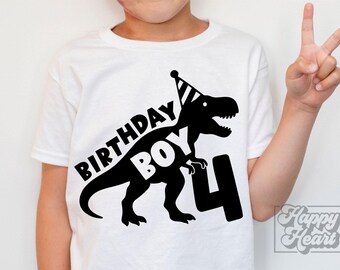 May include: White t-shirt with a black dinosaur graphic wearing a party hat, the words "BIRTHDAY BOY" and the number "4". A child is wearing the shirt and giving a peace sign.