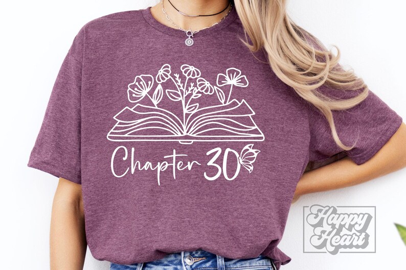 May include: A purple t-shirt with a white design of an open book with flowers growing out of it. The text "Chapter 30" is below the book with a butterfly to the right of the number.