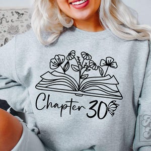 May include: A gray sweatshirt with a black graphic of an open book with flowers growing out of it. The text "Chapter 30" is below the book with a butterfly to the right.