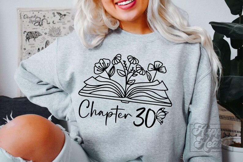 May include: A gray sweatshirt with a black graphic of an open book with flowers growing out of it. The text "Chapter 30" is below the book with a butterfly to the right.