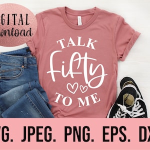Könnte beinhalten: Ein pinkfarbenes T-Shirt mit dem Text "TALK Fifty TO ME" in Weiß. Das Shirt ist gefaltet und auf einer weißen Oberfläche mit einer blauen Jeans und schwarzen Turnschuhen abgelegt.