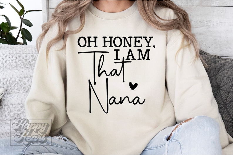K&ouml;nnte beinhalten: Ein cremefarbener Pullover mit dem Text "Oh honey, I am that Nana" in schwarzer Schrift mit einem kleinen schwarzen Herz.