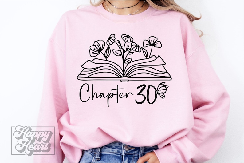 May include: A pink sweatshirt with a black graphic of an open book with flowers growing from it. The text "Chapter 30" is below the book with a butterfly to the right.