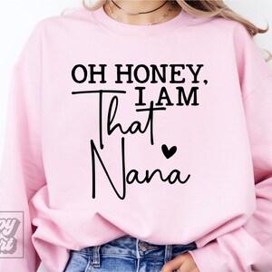 K&ouml;nnte beinhalten: Rosafarbener Pullover mit dem Text "Oh honey, I am that Nana" in Schwarz mit einem kleinen schwarzen Herz.