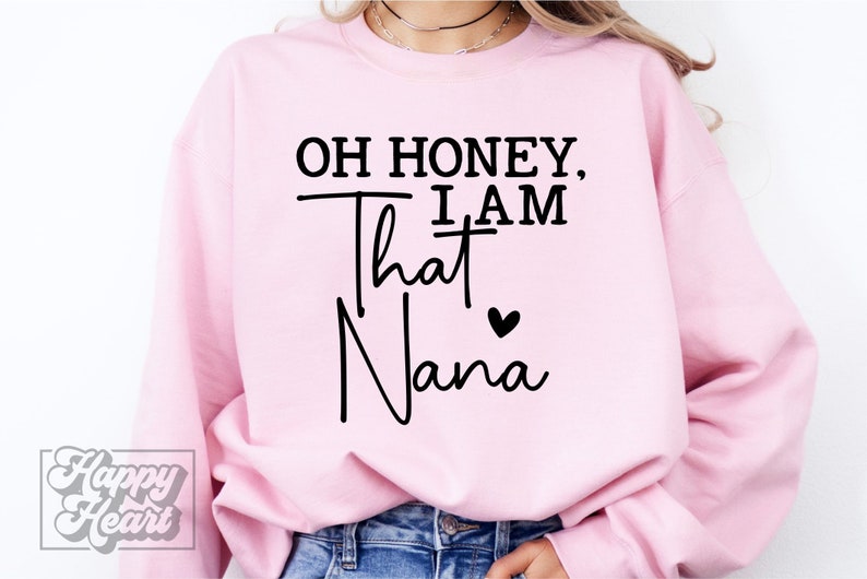 K&ouml;nnte beinhalten: Rosafarbener Pullover mit dem Text "Oh honey, I am that Nana" in Schwarz mit einem kleinen schwarzen Herz.