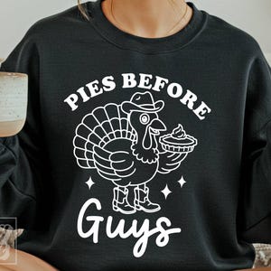 May include: Black sweatshirt with a white graphic of a turkey wearing a cowboy hat and boots, holding a pie. The text "PIES BEFORE GUYS" is above and below the turkey illustration. A white mug is held in the left hand.