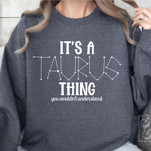 Puede incluir: Sudadera gris con el texto "It's a Taurus thing you wouldn't understand" en blanco. La palabra "Taurus" está formada por estrellas blancas.