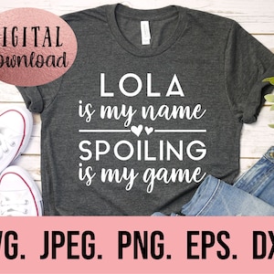 May include: A grey t-shirt with white text that reads "LOLA is my name SPOILING is my game". There are two small hearts above the word "SPOILING".
