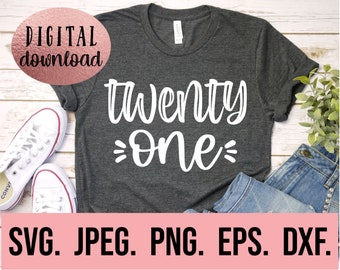 May include: A dark gray t-shirt with the text "twenty one" in white cursive lettering. The shirt is displayed on a wooden surface with a pair of white sneakers and blue jeans.