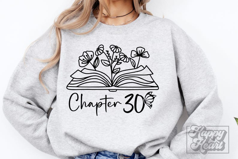 May include: A gray sweatshirt with a black and white design of an open book with flowers growing out of it. The text "Chapter 30" is below the book with a butterfly to the right of the number.