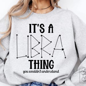 May include: A light gray sweatshirt with the text "IT'S A LIBRA THING you wouldn't understand" in black. The word "LIBRA" is designed as a constellation. The sweatshirt has long sleeves.