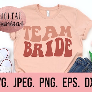 Peut inclure: Un t-shirt rose avec le texte "TEAM BRIDE" dans un style de police rétro. Le texte est dans des tons de rose et de rouge.