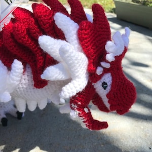 May include: A crocheted dragon toy with red and white yarn. The dragon has a long snout and a spiky back.