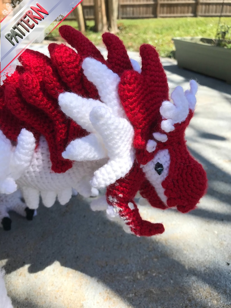 May include: A crocheted dragon toy with red and white yarn. The dragon has a long snout and a spiky back.