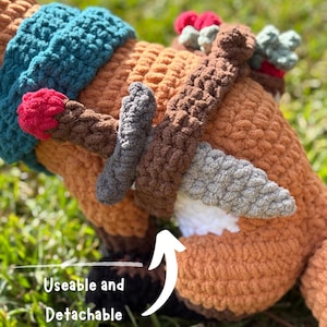 K&ouml;nnte beinhalten: Geh&auml;keltes Pl&uuml;schtier in Braun-, T&uuml;rkis- und Graut&ouml;nen mit roten und gr&uuml;nen Akzenten. Das Spielzeug hat ein strukturiertes Aussehen und verf&uuml;gt &uuml;ber abnehmbares Zubeh&ouml;r. Das Wort "PATTERN!" ist sichtbar, und "Useable and Detachable Accessories" steht unten links.