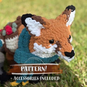 Puede incluir: Un juguete de zorro tejido a ganchillo con una cara marrón, blanca y negra, que lleva un chaleco azul verdoso. El zorro está hecho de un hilo suave y texturizado. La imagen incluye el texto "PATTERN! + ACCESSORIES INCLUDED".