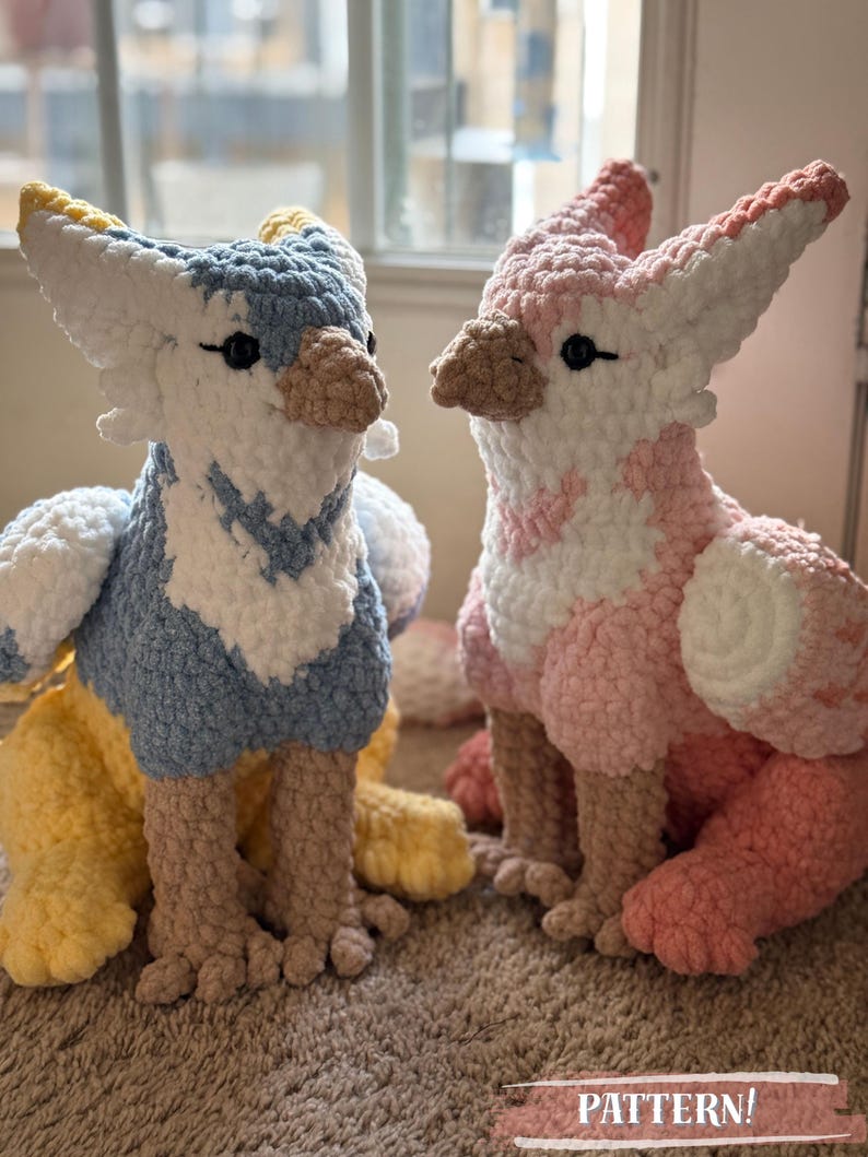 May include: Two handmade crochet gryphon plushies. One is blue, white, and yellow, the other is pink and white. They have detailed wings, beaks, and feet. The word "PATTERN!" is visible at the bottom.