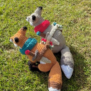 K&ouml;nnte beinhalten: Zwei geh&auml;kelte Fuchs- und Eichh&ouml;rnchen-Pl&uuml;schtiere auf gr&uuml;nem Gras. Der Fuchs ist orange und braun mit einem t&uuml;rkisfarbenen Schal, und das Eichh&ouml;rnchen ist grau mit einem roten Schal. Der Text "PATTERN!" steht oben.