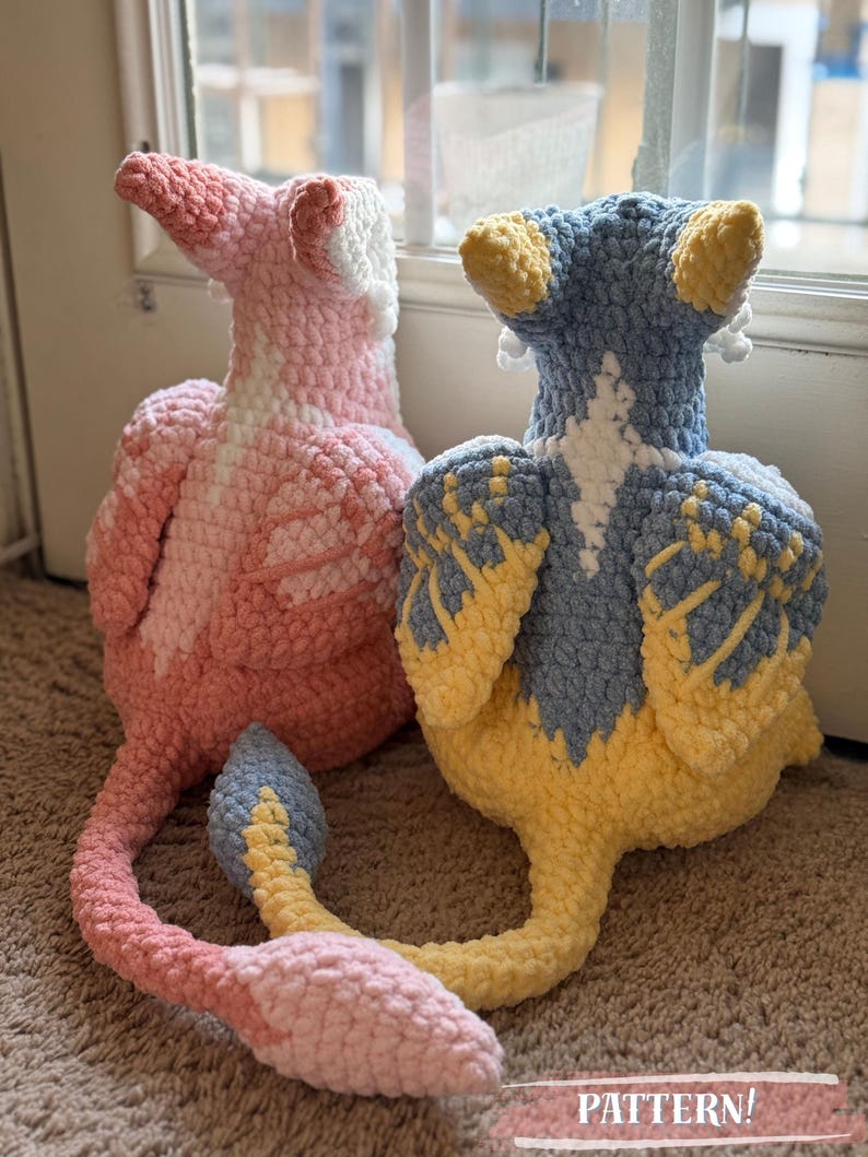May include: Two handmade crochet plush toys. One is pink and white, the other is blue and yellow. Both have long tails and are sitting on a brown carpet. The text "PATTERN!" is visible at the bottom.