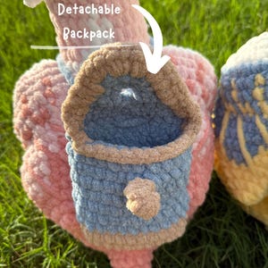 May include: Close-up of a handmade crochet item with a detachable backpack. The item is primarily pink, with a blue and tan backpack. The text "Useable and Detachable Backpack" and "PATTERN!" are visible.