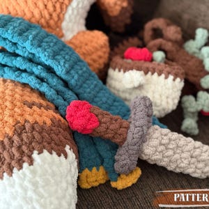 K&ouml;nnte beinhalten: Geh&auml;keltes Fuchspielzeug mit blauem Schal, Schwert und Kuchen. Der Fuchs ist orange, braun und wei&szlig;. Das Schwert ist grau, braun und rot. Der Kuchen ist wei&szlig; und braun. Das Wort "PATTERN!" ist im Bild.