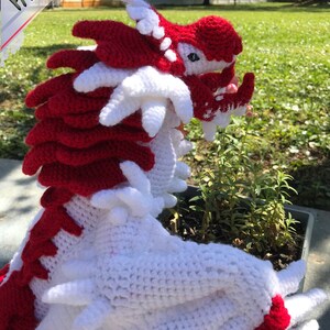 May include: A crocheted dragon toy with white and red yarn. The dragon has a spiky back and a long tail.