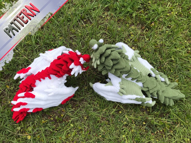 May include: Two crocheted dragons, one red and white and one green and white, are lying on a bed of green grass.