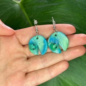Peut inclure: Une paire de boucles d'oreilles en forme de demi-cercle en argile polymère, de couleur bleu et vert avec des points noirs.