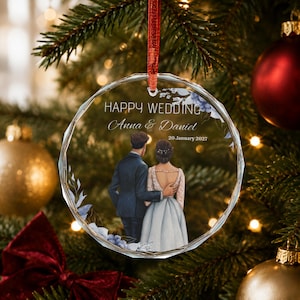 Puede incluir: Un adorno de cristal circular facetado con una ilustración impresa de una pareja vista desde atrás, con el texto HAPPY WEDDING, Anna & Daniel y 20 January 2027. El diseño incluye detalles florales azules y cuelga de una cinta roja.