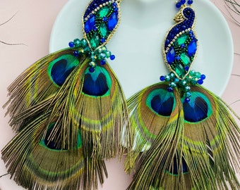 May include: A pair of peacock feather earrings with blue and green beaded peacocks. The earrings are approximately 6 inches long.