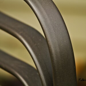 May include: Close-up of a black metal chair with curved, rounded arms. The chair is made of multiple pieces of metal that are welded together.