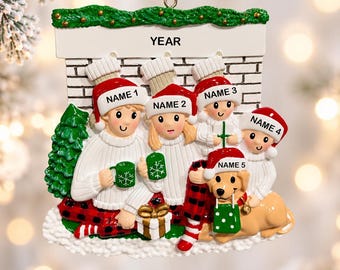 May include: A personalized Christmas tree ornament shaped like a fireplace mantel with five family members and a dog. Each figure wears a red Santa hat and white sweater. The mantel features the text YEAR and spaces for five names.